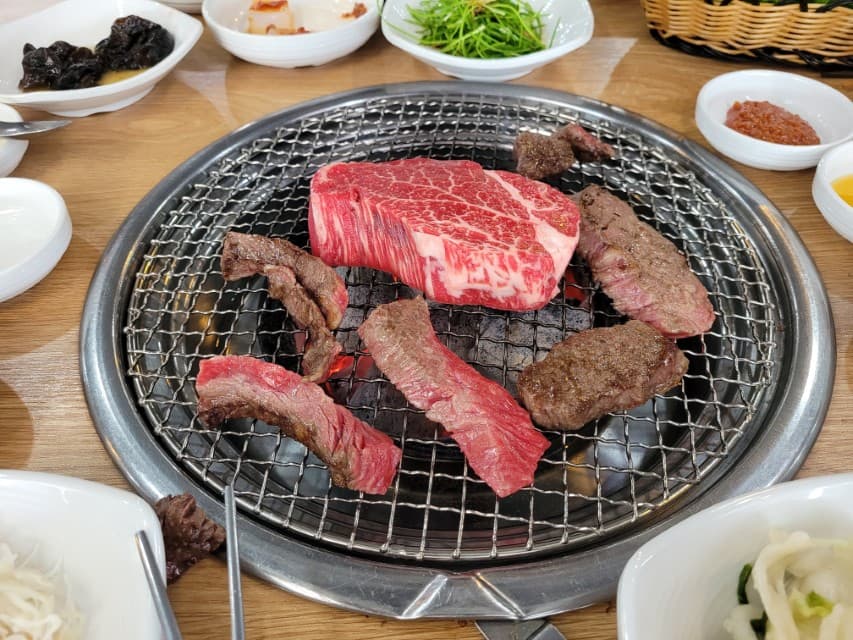 숯불 불판 위 신선한 한우와 익어가는 소고기 구이 반찬들