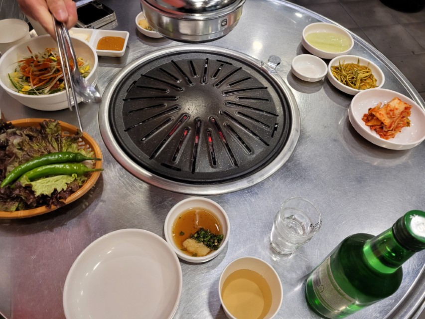 뜨거운 고기 불판, 신선한 야채, 김치, 소주 병.