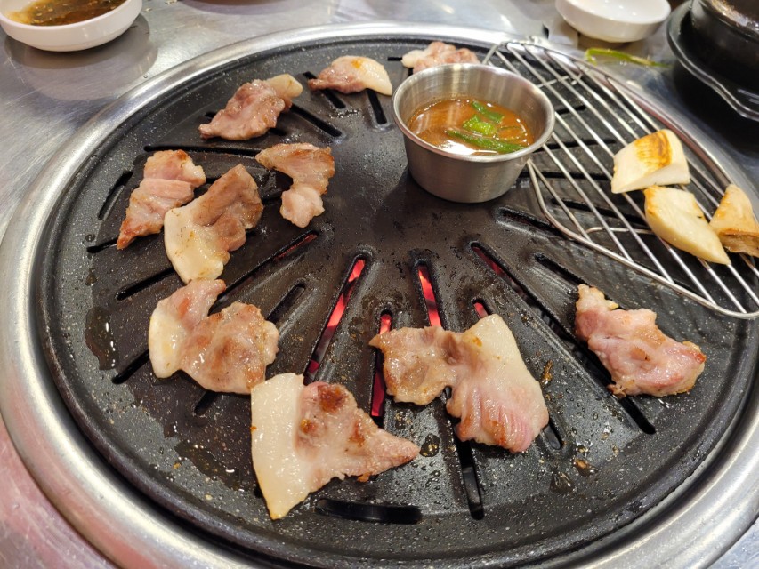 뜨거운 불판 위 노릇하게 구워지는 삼겹살, 소스, 버섯.
