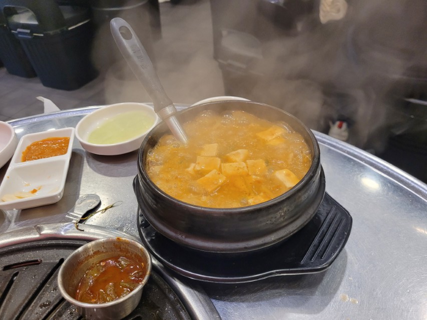 김 솟아오르는 뜨거운 두부찌개 뚝배기, 국자, 여러 반찬