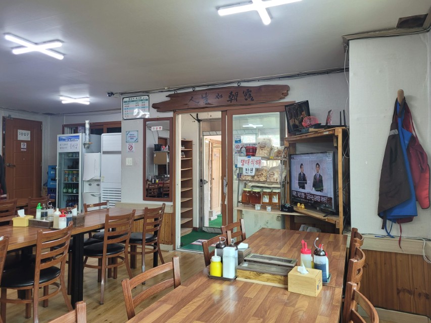 편안한 한식당 실내, 나무 식탁, TV, 음료 냉장고, 명태식해 판매.
