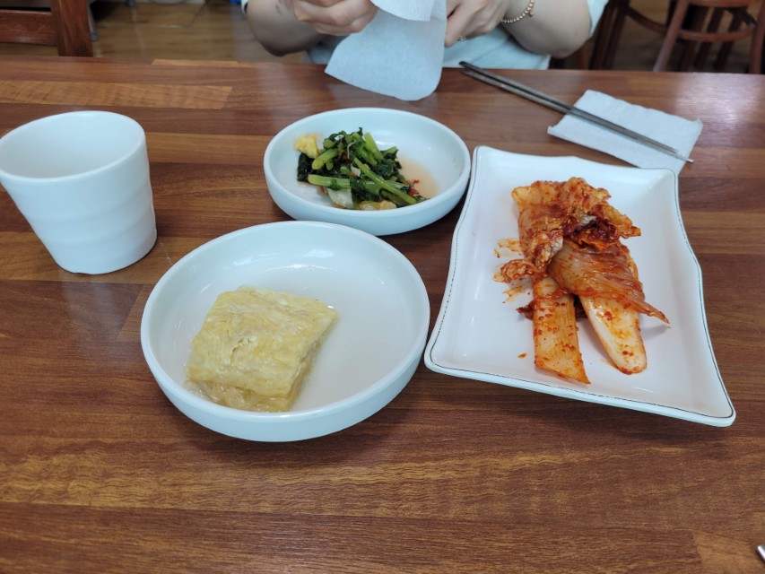 나무 식탁 위 김치, 계란말이, 나물 반찬, 컵