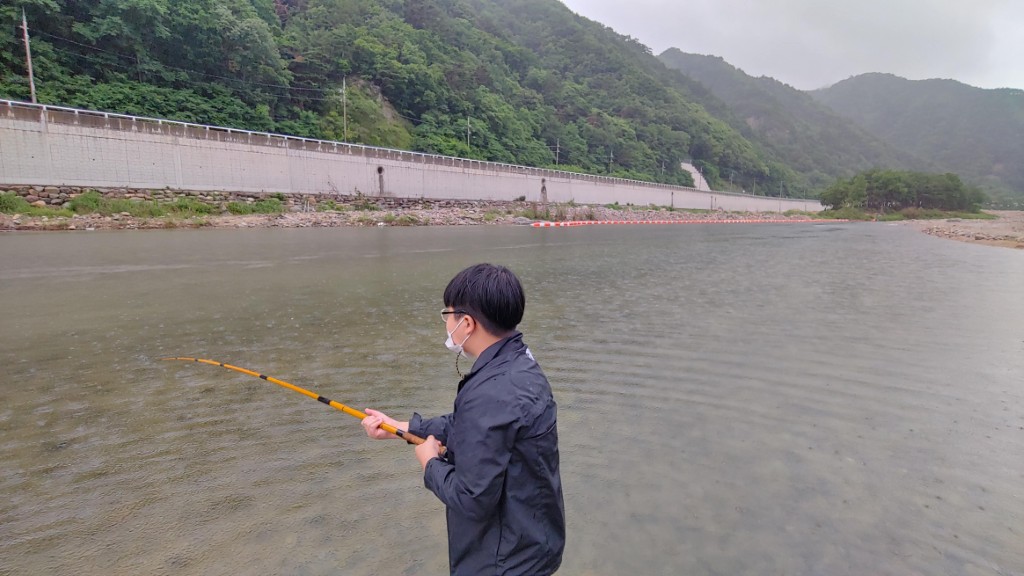 비 내리는 흐린 강물, 우비 입고 낚싯대 들고 낚시
