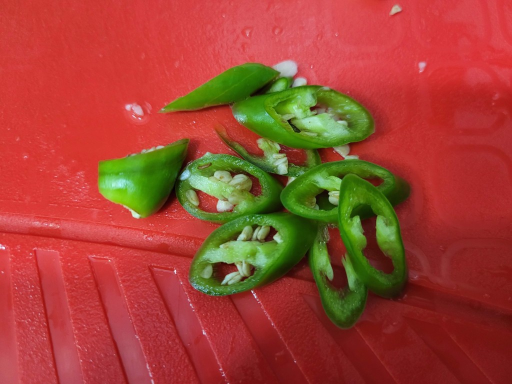 빨간 도마 위 신선한 청고추 썰린 조각들, 씨앗 보임.