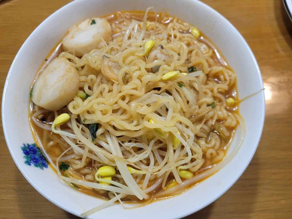 매콤한 해물 라면, 가리비, 콩나물 듬뿍 담긴 흰 그릇