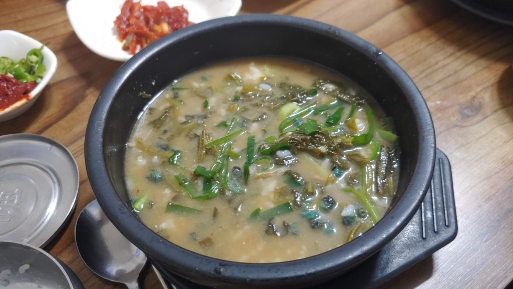 검은 뚝배기 다슬기 들깨탕 푸른 채소 나무 탁자