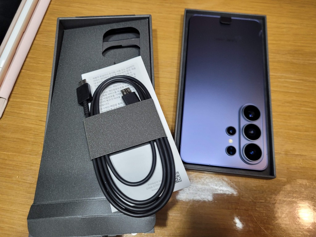 개봉된 보라색 스마트폰, 여러 카메라, USB-C 케이블, 박스
