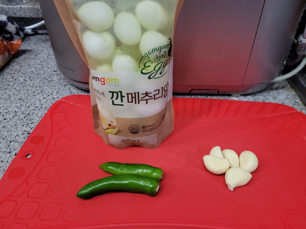 붉은 도마 위 깐메추리알 봉지, 풋고추, 통마늘 재료