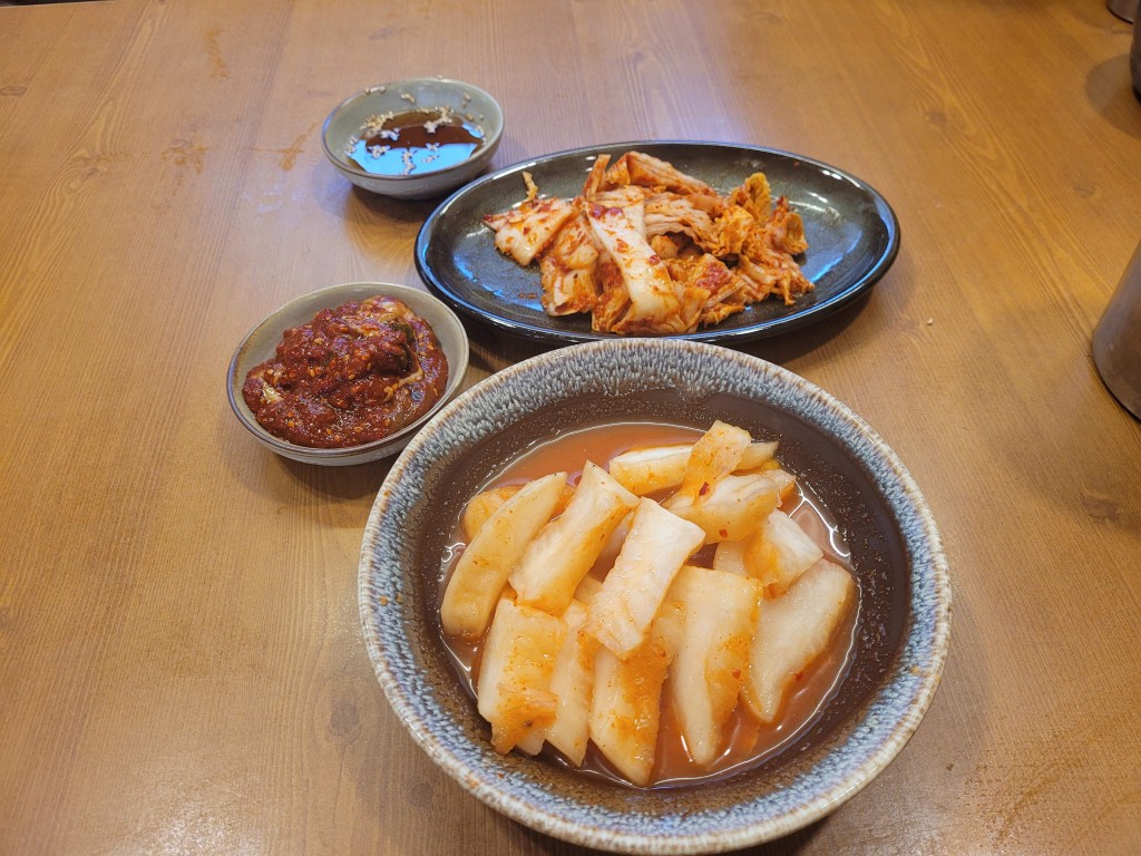 나무 식탁 위 다양한 한국 반찬, 깍두기, 배추김치, 매운 양념, 간장