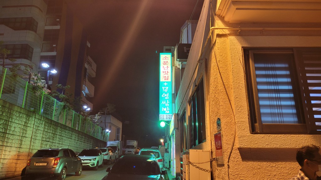 빛나는 소문난맛집 무영쌈밥 간판, 좁은 길가 주차된 차량