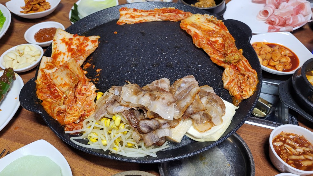 불판 위 삼겹살, 김치, 콩나물, 두부, 다양한 한식 반찬
