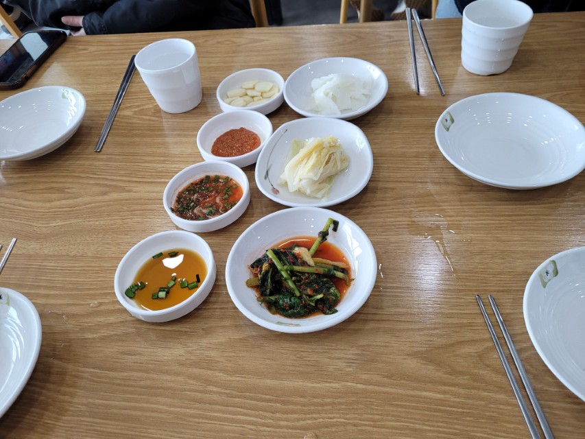 나무 식탁 위 한식 반찬, 김치, 소스, 마늘, 컵, 젓가락