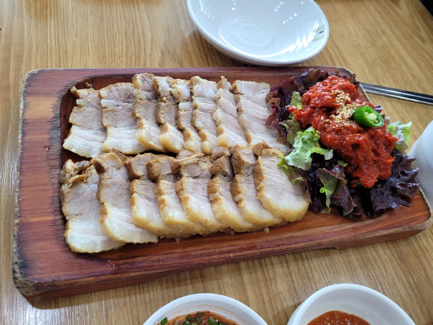 나무 쟁반 위 썰린 보쌈, 매콤한 김치, 신선한 상추
