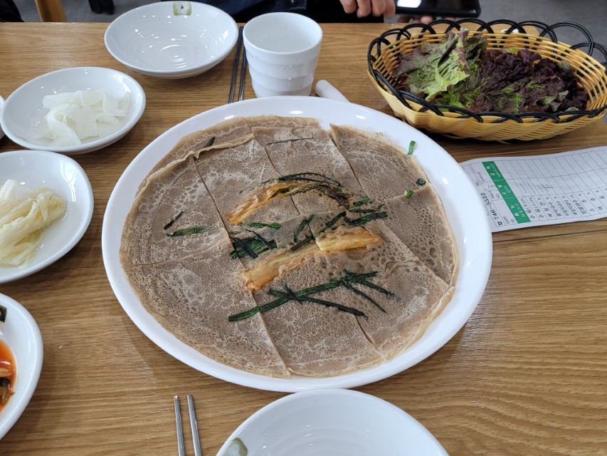 김치와 파 고명 얹은 메밀전병, 나무 식탁 위 한식 상차림.