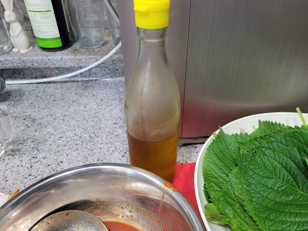 신선한 깻잎 더미, 노란 뚜껑 들기름병, 붉은 양념장 그릇
