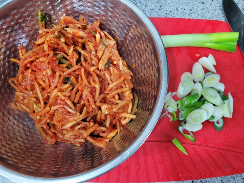 금속 그릇 붉은 무생채, 빨간 도마 위 썰린 파 칼.