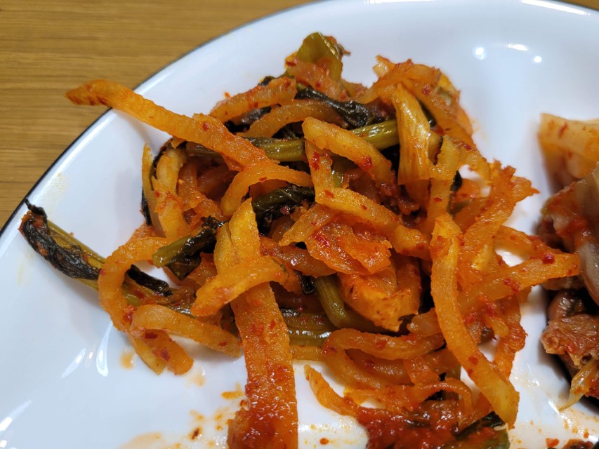 흰 접시 위 주황색 매콤한 무생채, 녹색 채소 섞임