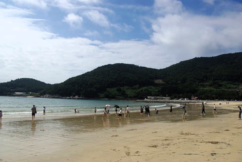 녹색 산 둘러싼 푸른 바다 해변, 여럿 물가에서 놀이