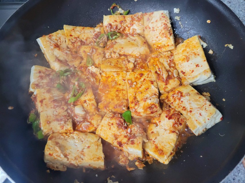 두부 조림 조각 매운 빨간 양념, 녹색 고추, 김 나는 검은 프라이팬.