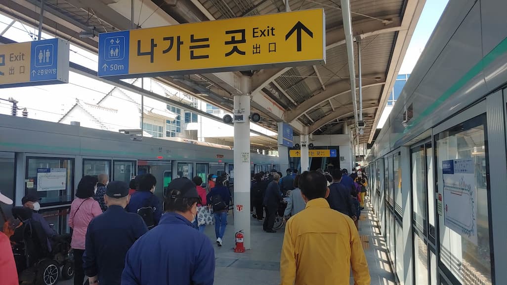 지하철 승강장, 노란색 출구 표지판, 열차 정차, 많은 통행객