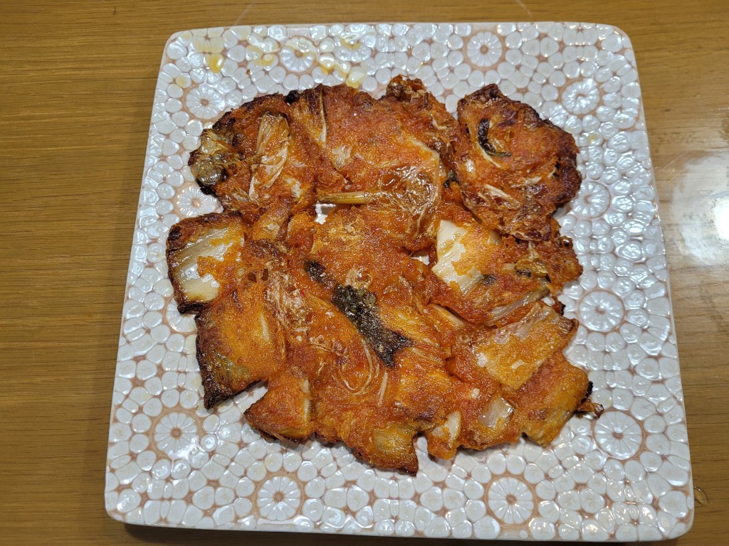 노릇하게 구워진 황금빛 생선전, 무늬 접시 위 나무 식탁