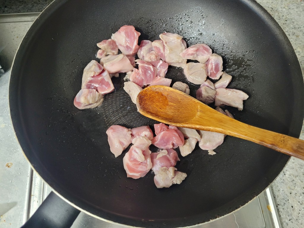 검은 프라이팬에서 분홍색 돼지고기 조각을 나무 주걱으로 볶는 중