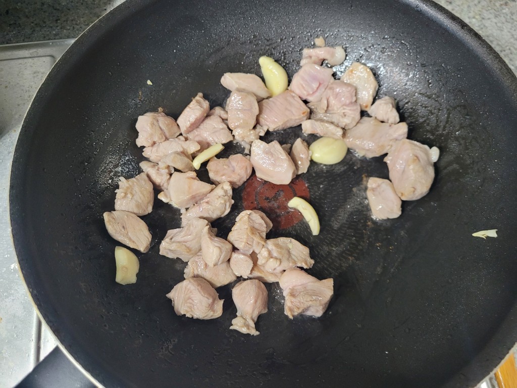 검은 팬에 깍둑썰기 고기와 통마늘 노릇하게 볶는 요리.