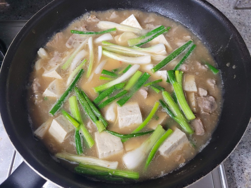 팬에서 두부, 대파, 고기 넣은 찌개 끓는 중