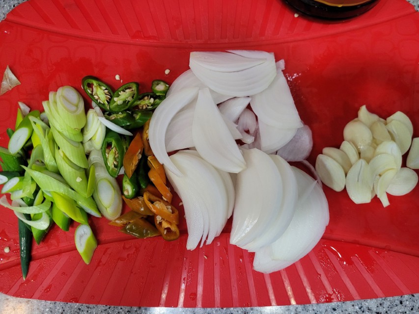 빨간 도마 위 썰어 놓은 파, 고추, 양파, 마늘