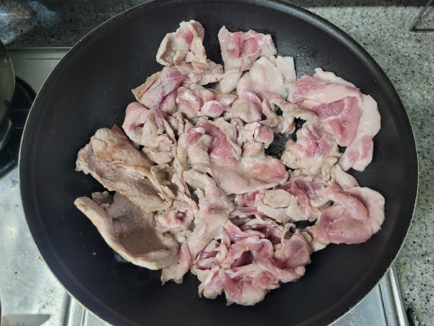 검은색 팬 위 익어가는 얇게 썬 돼지고기 조각들