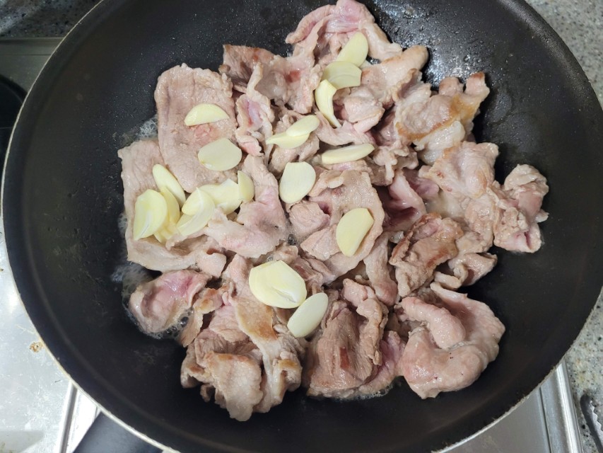 검은 프라이팬 속 얇은 돼지고기 조각과 마늘 슬라이스 볶는 중