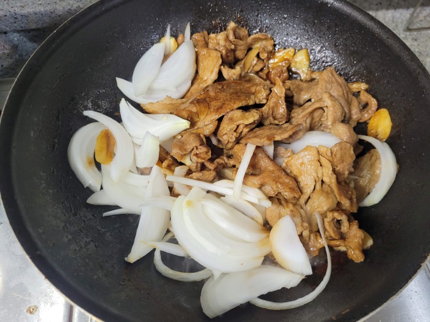 프라이팬에 갈색 고기, 흰 양파, 마늘 볶음 조리 중