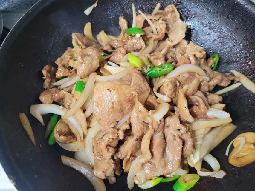 검은 팬에 양파, 풋고추와 함께 볶는 고기 요리