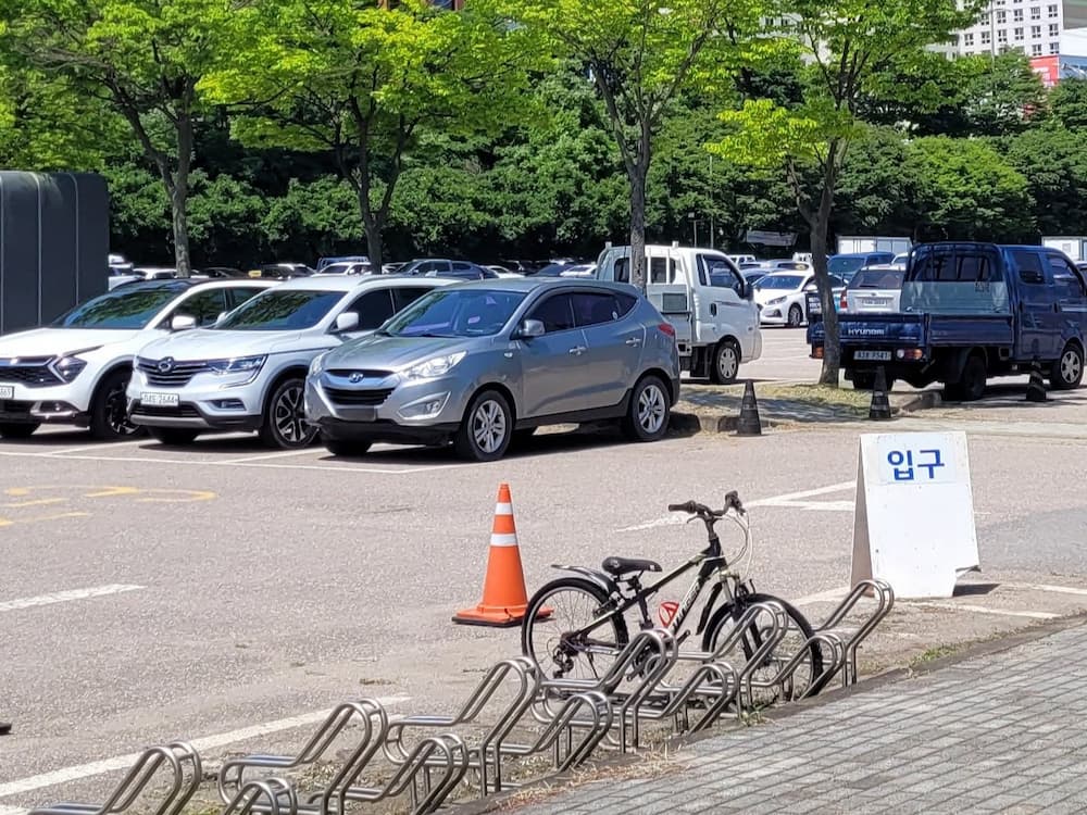 주차장, 다양한 차량, 자전거, 입구 표지판, 푸른 나무