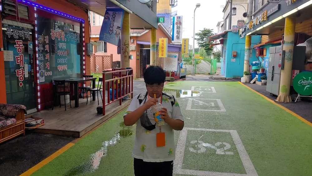 청소년 젖은 초록 길 음료 마심, 다채로운 상점 배경