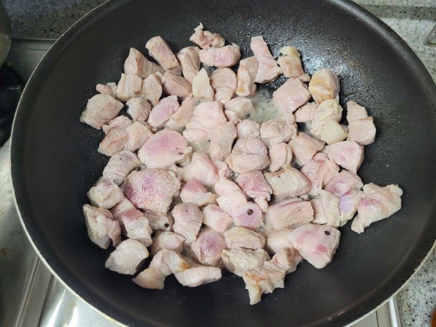 프라이팬에 깍둑썬 돼지고기 조리, 연분홍 고기 노릇하게 익어감.