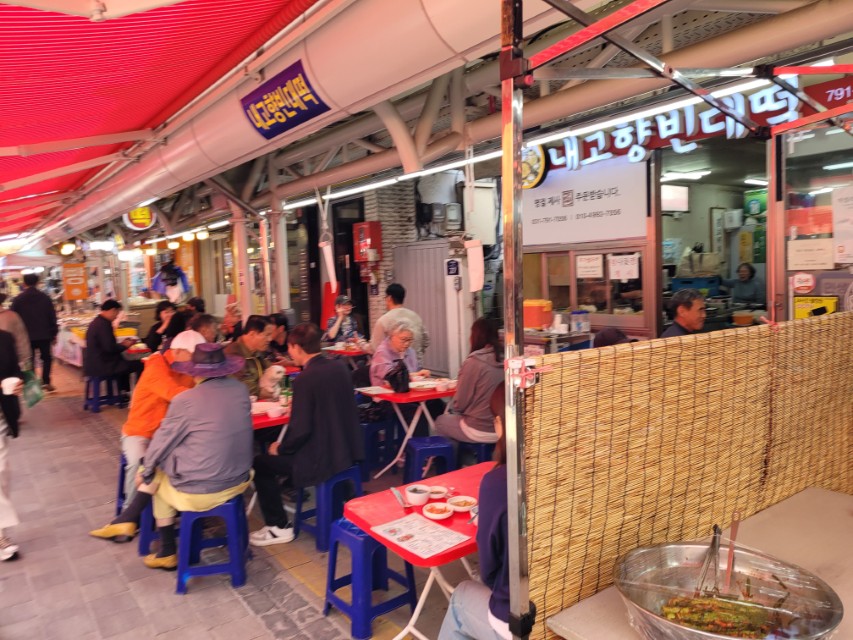 내고향빈대떡 시장 노점, 식사 풍경, 빨간 차양, 파란 의자.