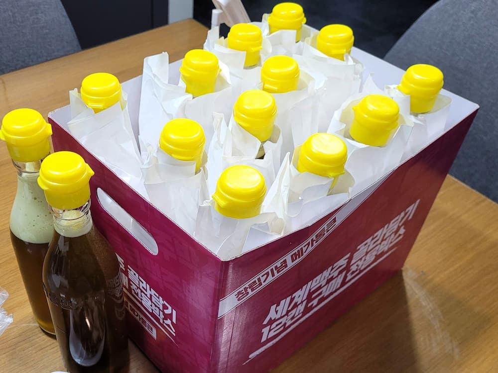 노란색 뚜껑 갈색 병 맥주 12개 포장 상자, 두 병 옆에.