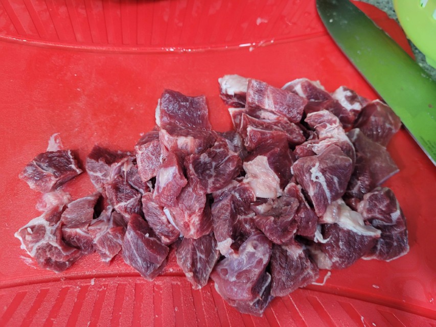 빨간 도마 위 깍둑썰기 된 생붉은 육류 조각, 녹색 칼.