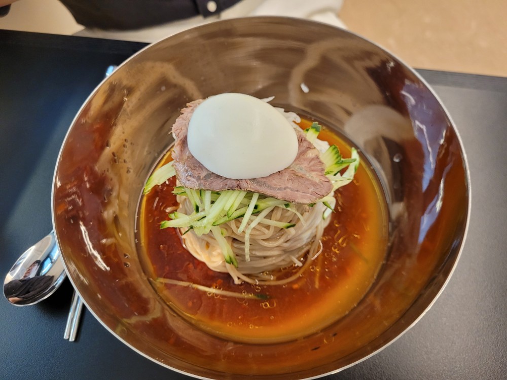 스테인리스 그릇, 붉은 육수, 소고기, 오이, 삶은 달걀 올린 냉면