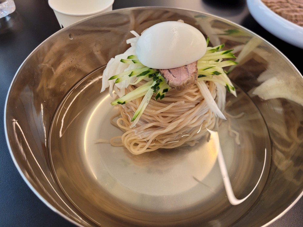 은색 그릇 물냉면, 투명 국물, 삶은 달걀, 오이, 무, 고기 고명