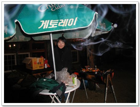 게토레이 우산 아래 웃는 얼굴, 밤 바비큐 그릴에서 연기 피어오름.