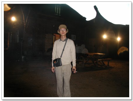 모자 안경 착용자, 야간 건물 앞 담배 들고 미소 짓는다
