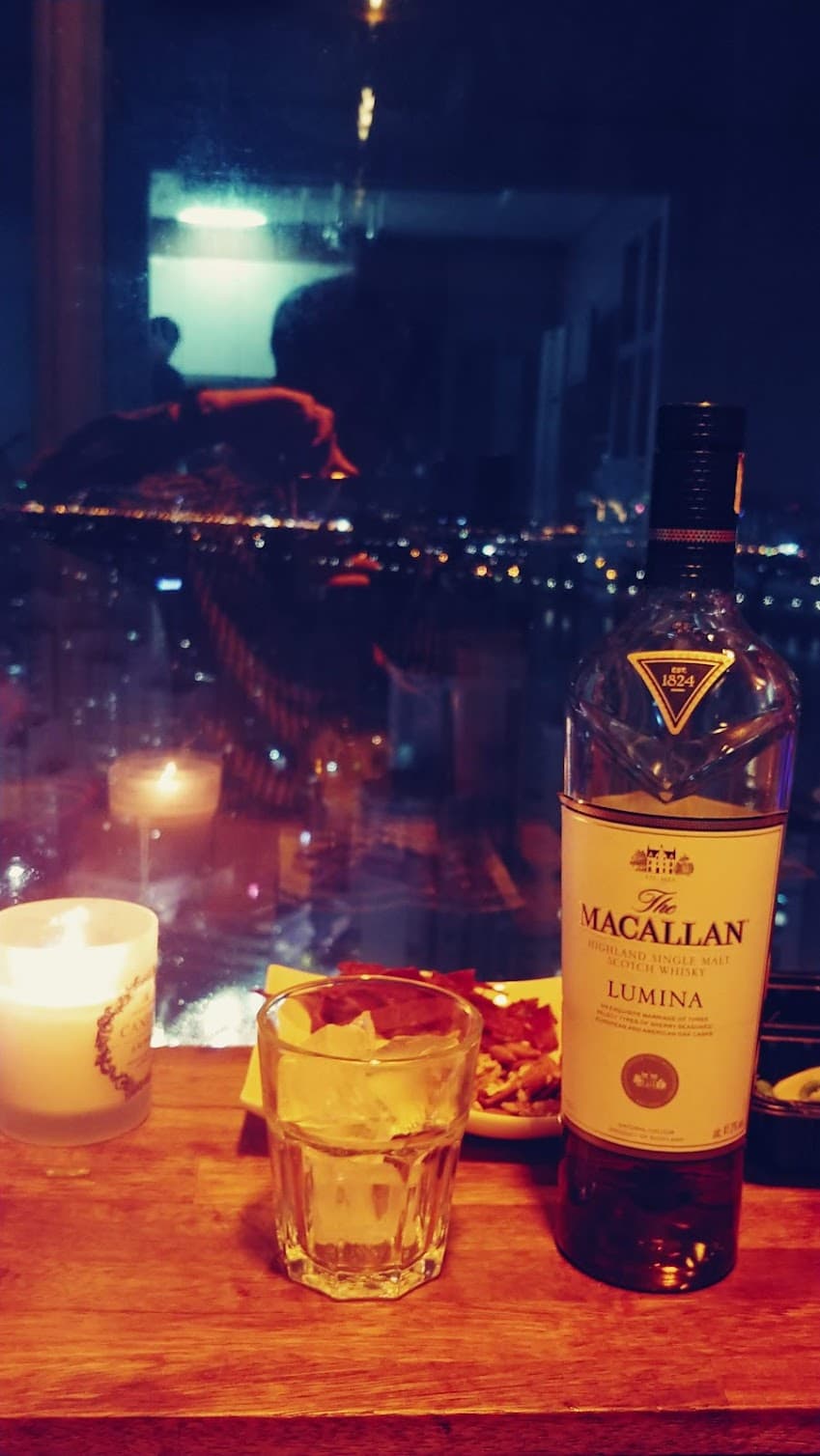 맥캘란 루미나 위스키 병, 얼음 잔, 양초, 고층 도시 야경