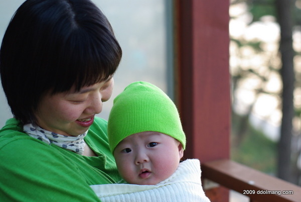 웃는 어머니 녹색 모자 아기 안고 있음 야외 배경