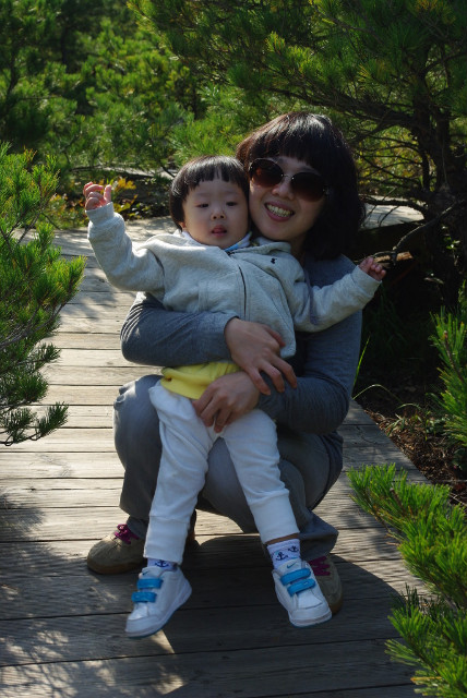 어머니와 아이 햇살 비추는 나무 데크 위 푸른 숲 배경