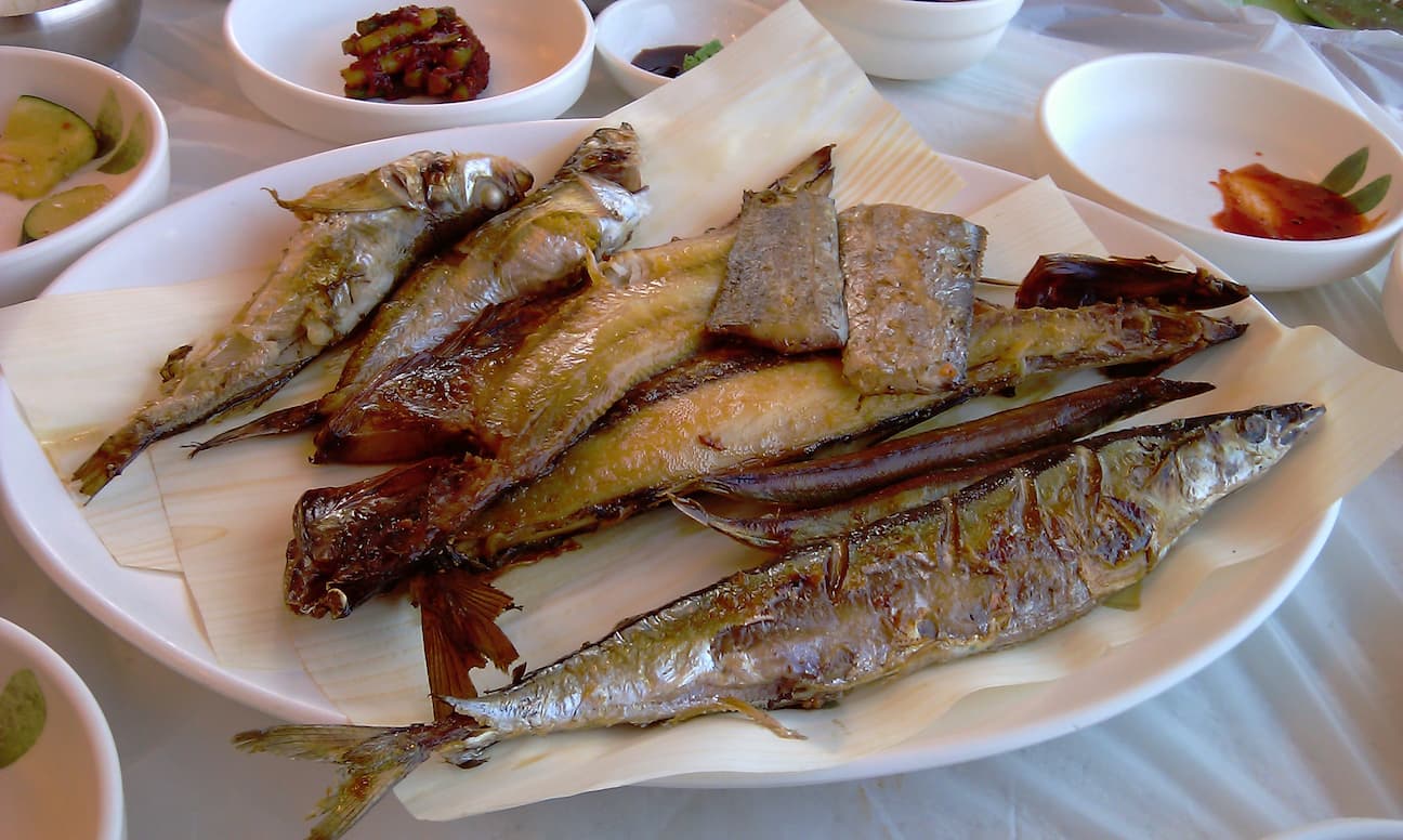 흰 접시, 노릇하게 구운 통 생선 여러 마리, 다양한 반찬