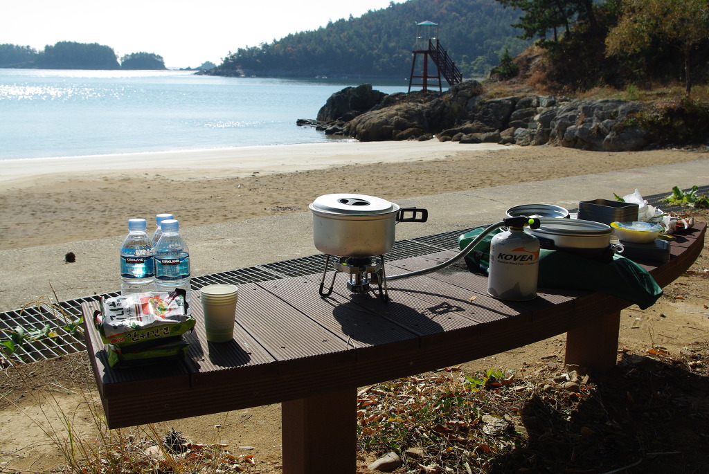 해변 벤치 위 캠핑 장비, 냄비, 버너, 물, 라면.