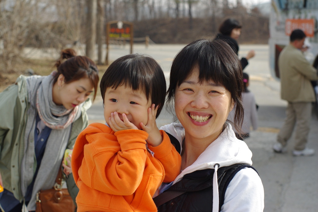 밝게 웃는 어머니, 주황색 후드티 입은 아이 입 가린 채