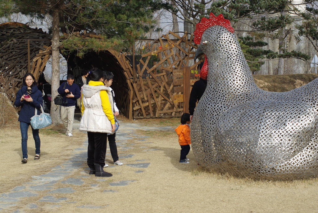 붉은 볏 금속 닭 조형물, 나무 터널, 어린아이와 관람객들
